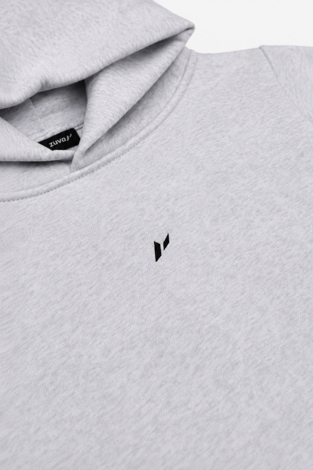 Zuva Grey Hoodie close-up detail — embroidered black Zuva icon on ash grey marl heavyweight fleece with woven neck label