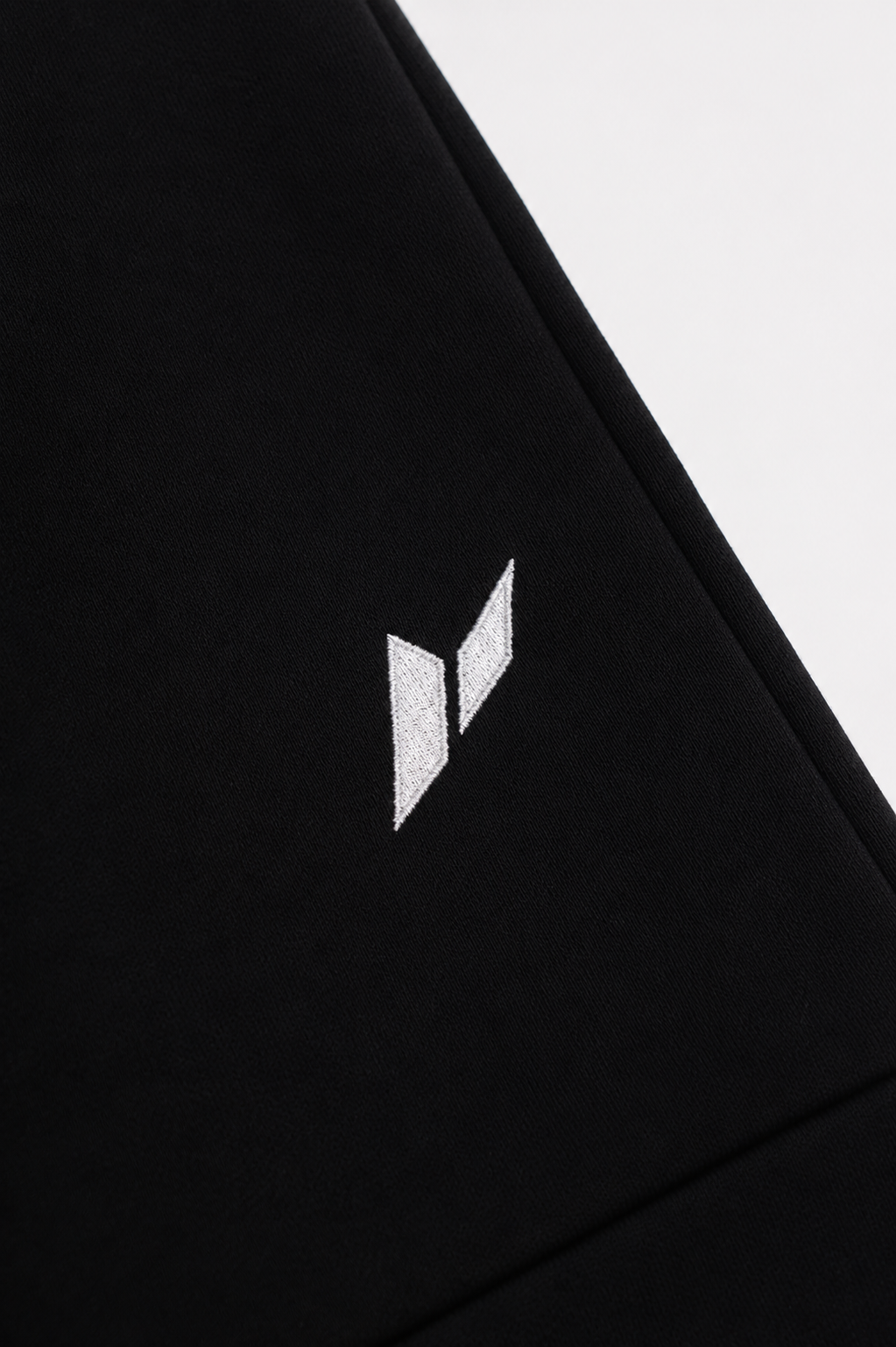 Zuva Black Track Pants close-up embroidered logo detail — white Zuva icon stitched on black heavyweight fleece mens athletic track pants Australia
