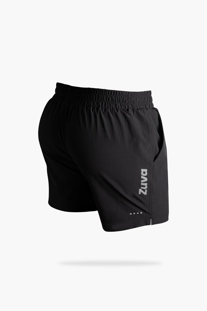 Rear view of black men's athletic shorts featuring the Zuva logo printed vertically on the side, with elastic waistband and subtle reflective dots near the hem.